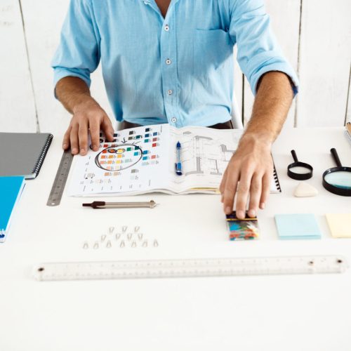 Hands of young businessman sitting at table with notepad. White modern office background.